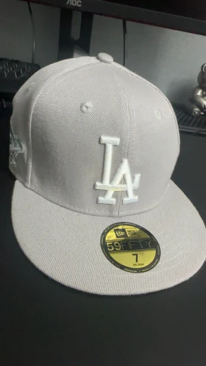 Grå LA Dodgers 59FIFTY keps - Snygg grå LA Dodgers 59FIFTY keps från New Era med broderad LA-logga i vitt framtill och 1988 World Series-detalj på sidan. Platt skärm och klassisk passform. Materialet är bomull och polyester, insidan har svarta band med 59FIFTY-tryck. Kontakta gärna för funderingar🤩