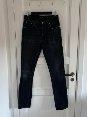 Svarta jeans från Nudie Jeans Co W30 L34 - Säljer ett par svarta jeans från Nudie Jeans Co i storlek W30 L34. Jeansen har klassisk femficksdesign, svarta broderade detaljer på bakfickorna och en mörk tvätt med lätt slitning. Passformen är rak och materialet är slitstarkt denim. !! Patch påsydd på högra knäet och hål i vänstra fickan!!