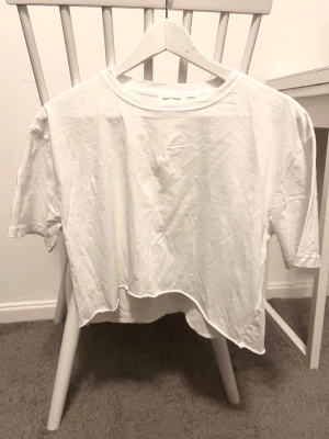 Vit croppad t-shirt - Säljer en vit croppad t-shirt med korta ärmar och rund hals. T-shirten har en asymmetrisk nederkant som ger en cool och avslappnad vibe. Perfekt för dig som gillar enkel och stilren design.