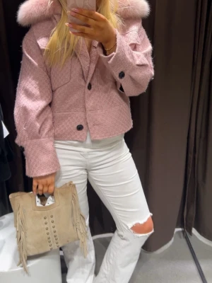 Rosa teddyjacka med pälskrage från Meotine - Superfin rosa teddyjacka från Meotine med stor fluffig pälskrage. Jackan har två stora bröstfickor, knappar framtill och en croppad passform. Materialet är ullmix med detaljer i äkta päls, perfekt för dig som vill sticka ut med en mysig och trendig look.