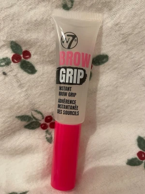 W7 Brow Grip ögonbrynsgel - W7 Brow Grip är en transparent ögonbrynsgel som ger direkt stadga till brynen. Kommer i en smidig tub med rosa lock och svart/vit/rosa text. Perfekt för att forma och fixera brynen hela dagen. Enkel att applicera med medföljande borste.