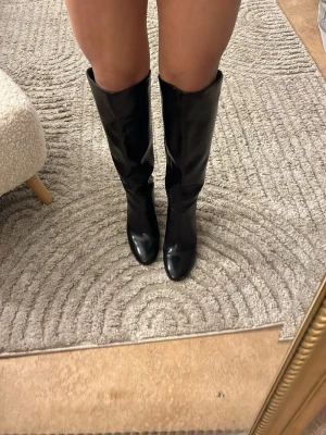 Svarta höga boots med klack - Säljer ett par svarta höga boots med en hög klack. Skorna är gjorda i glansigt skinnmaterial och om passar till många outfits. Säljs då jag har en massa andra boots och att jag inte använder dom. 💗