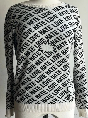 Vit stickad tröja med textmönster - Cool vit stickad tröja med svart textmönster där det står 'LOVE' och 'HATE' över hela plagget. Tröjan har rund hals, långa ärmar och ribbade muddar vid ärmslut och nederkant. Perfekt för dig som gillar statement-plagg och grafiska prints.