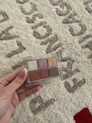 CAIA Disco Fever ögonskuggspalett - Säljer en CAIA Disco Fever ögonskuggspalett med sex skimrande nyanser: champagne, lila, guld, koppar, rosé och brons. Paletten har ett genomskinligt plastfodral och varje skugga har ett eget namn. Perfekt för att skapa kreativa och glittriga looks.