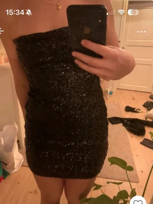 Svart paljettklänning axelbandslös - Säljer en svart, axelbandslös kortklänning täckt av glittriga paljetter. Klänningen har en tight passform och är perfekt för dig som vill sticka ut. Den är kort och sitter snyggt på kroppen, vilket ger en festlig och trendig look.