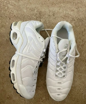 Nike vita sneakers Air Max - Säljer ett par fräscha vita Nike Air Max sneakers med snygg vågig design och synlig luftdämpning i sulan. Skorna har snörning och är tillverkade i mesh och syntetmaterial för en sportig look. Perfekta för dig som gillar stilrena och bekväma sneakers.