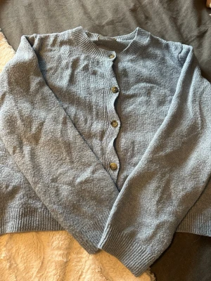 Ljusblå kofta från MNG med knappar - Mysig ljusblå kofta från MNG med rund halsringning och ribbade muddar. Tröjan har långa ärmar och stängs med knappar framtill. Perfekt att slänga över en topp när det blir kyligt.