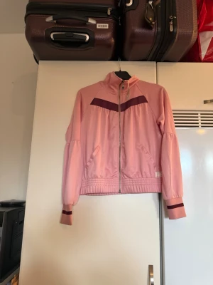 Odd Molly Rose Run jacka rosa - Säljer en snygg rosa vindjacka från Odd Molly i modellen Rose Run. Jackan har dragkedja framtill, ribbade muddar med mörkare rand, hög krage och två fickor. Materialet är mjukt och lätt, perfekt för vår och sommar. Färgen är bridal rose med en mörkare detalj över bröstet. Storlek 1 som enligt deras storleksguide motsvarar en storlek S. Helt ny med tags. 