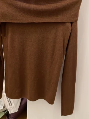 Brun offshoulder topp - Säljer en brun offshoulder topp med lång ärm och bred kant upptill. Toppens material är mjukt och stretchigt, troligen stickad eller bomull. Perfekt för dig som gillar stilrena och enkla plagg med en twist.