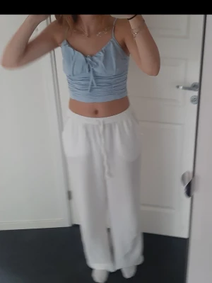 Ljusblå croppad linnetopp från Nelly - Säljer en ljusblå croppad linnetopp från Nelly i storlek S. Toppen har smala axelband, snygg snörning framtill och rynkade detaljer som ger en cool look. Perfekt för varma dagar och enkel att matcha med jeans eller kjol.