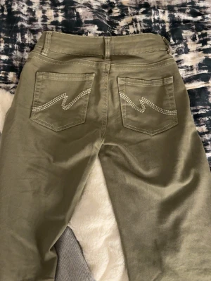Bootcut byxor i grön  - Snygga gröna bootcut-byxor med två bakfickor som har dekorativa sömmar i zigzag-mönster. Byxorna har låg midja. Använd fåtal gånger alltså nytt skick 🥰