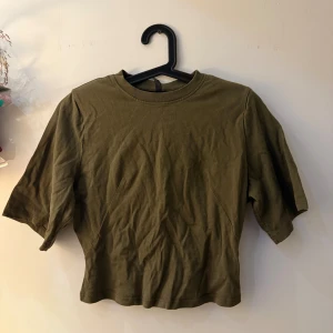 Olivgrön croppad topp från H&M Divided - Säljer en olivgrön croppad topp från H&M Divided i storlek XS. Toppen har rund hals, korta ärmar och är tillverkad i mjuk bomull. Enkel och clean design som är lätt att matcha med jeans eller kjol. Perfekt för dig som gillar basic med lite edge.