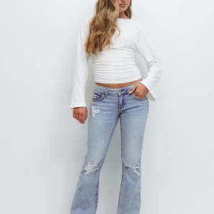 Bootcut jeans från Gina Tricot, ljusblå - Snygga ljusblå bootcut jeans från Gina Tricot i storlek 164. Jeansen har slitna detaljer och hål på benen för en cool look. Klassisk femficksmodell med knapp och dragkedja framtill. Perfekt för dig som gillar retrovibbar och avslappnad stil.
