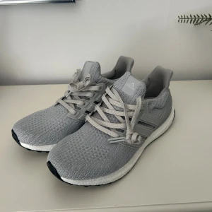 Grå Adidas Ultraboost sneakers - Snygga grå Adidas Ultraboost sneakers med stickad ovandel och platt sula. Skorna har klassisk snörning och en vit, dämpad mellansula för extra komfort. Perfekta för dig som gillar stilrena och sportiga sneakers med modern design.