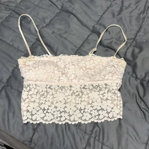 Beige spets tubtopp från H&M - Säljer en beige tubtopp från H&M i storlek 36. Toppen är axelbandslös med justerbara smala band och har ett vackert blommigt spetsmönster över hela plagget. 