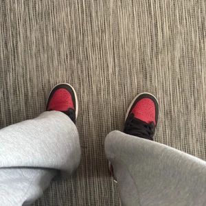 Nike Air Jordan 1 Low röd/svart - Säljer ett par Nike Air Jordan 1 Low sneakers i rött, svart och vitt. Skorna har klassisk snörning, rund tå och platt sula. Ikonisk Air Jordan-logga på hälen och vit swoosh på sidan. Materialet är skinn och syntet, perfekt för dig som gillar streetwear.