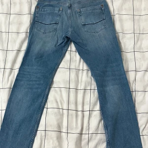 Blå straight jeans från Cross Jeans - Säljer ett par blå jeans från Cross Jeans, modell Antonio. De har regular waist och raka ben, klassisk femficksdesign och knappstängning. Materialet är bomull med lite elastan för extra komfort. Perfekt passform för dig som gillar avslappnad stil.