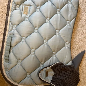 Ice blue schabrak från Equestrian Stockholm  - Schabrak och matchande huva från Equestrian Stockholm, i färgen Ice blue och storlek full på båda. Produkterna är i fint skick med finns  tecken av användning på schabraket. Tvättad men kan förekomma lite hästhår. Säljes endast tillsammans. Tänker mig 450 kr eller kom med bud☺️