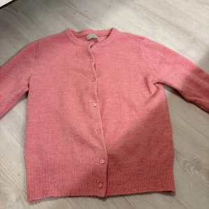 Rosa kofta från H&M i XS - Mysig rosa kofta från H&M i storlek XS. Koftan har rund halsringning, ribbade muddar och knäppning med matchande knappar framtill. Perfekt för lager-på-lager och enkel att styla till olika outfits.