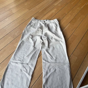 Beige kostymbyxor med raka ben - Snygga beige kostymbyxor med raka ben och klassisk passform. Byxorna har framfickor, bakfickor med knapp och stängs med dragkedja och knapp framtill. Perfekta för en clean och stilren look, tillverkade i mjukt bomullsmaterial.