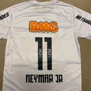 Vit Neymar Jr fotbollströja Santos M - Vit fotbollströja från Santos med Neymar Jr och nummer 11 på ryggen. Tryck med BMG och Netshoes, rund hals och korta ärmar. Tillverkad i lätt och ventilerande polyester, perfekt för dig som älskar brasiliansk fotboll.