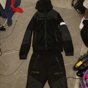 Nike Air Max svart tracksuit XS - Nike Air Max tracksuit i svart med dragkedja och huva. Snygga detaljer med AIR MAX-tryck på bröstet och ärmar i olika material. Perfekt för dig som gillar sportig och clean stil. Passar dig som vill ha en hoodie med modern look. Samma med byxorna. Köptes för 2500 i mall of scandinavia på jdsports.