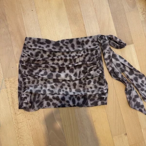 Leopardmönstrad omlottkjol med knyt S - Säljer en kort leopardmönstrad kjol med omlott-design och knyt i sidan. Kjolen har volangliknande lager och är i tunnt, mjukt material som ger en snygg draperad effekt. Färgerna går i beige och bruna toner, perfekt för dig som gillar djurmönstrat och vill sticka ut.