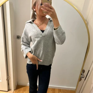 Grå stickad kofta med krage - Säljer en grå stickad kofta med bred krage och v-ringad hals. Tröjan har långärmade ärmar och en loose passform som ger en chill vibe. Perfekt att matcha med jeans eller kjol för en snygg look.