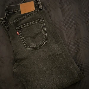 Levi's 501 jeans straight fit 30/30 - Svarta Levi's 501 jeans med klassisk straight fit och femficksdesign. Jeansen har den ikoniska läderpatchen bak i midjan och synliga nitar framtill. Tillverkade i robust denim med en snygg tvättad finish och normalhög midja. Perfekta för en clean och tidlös look. Toppen skick, inga skador. Storlek 30/30