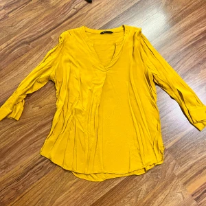 Gul blus från DeFacto med v-ringning - Säljer en snygg gul blus från DeFacto med v-ringning och långa ärmar. Blusen har en lös passform och är tillverkad i ett lätt, flowy material som ger en skön känsla. Perfekt för dig som gillar färg och vill sticka ut lite extra.