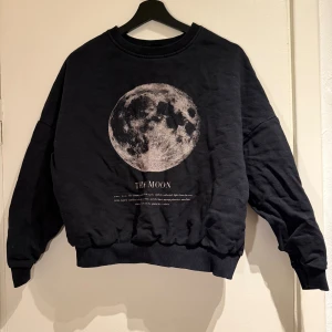 Svart sweatshirt med måne från Even&Odd - Cool svart sweatshirt från Even&Odd med stort tryck av månen på bröstet och text under. Tröjan har rund hals, ribbade muddar och en loose passform. 