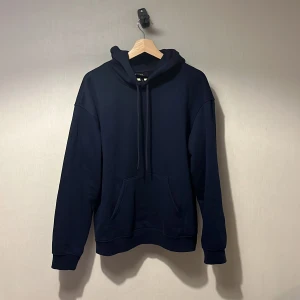 Mörkblå hoodie  - Snygg mörkblå hoodie från H&M i relaxed fit. Tröjan har huva med snörning, stor magficka och långa ärmar med ribbade muddar. Perfekt för chill dagar och enkel att matcha med jeans eller joggers.