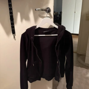 Svart velour hoodie Juicy Couture - Svart hoodie från Juicy Couture i mjuk velour med dragkedja framtill och huva. Klassisk modell med fickor och långa ärmar, perfekt för en chill och trendig look.