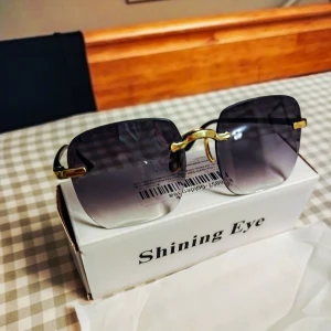 Helt nya Golden Tea-solglasögon kantlösa lilatonade glas - Golden Tea-solglasögon med en ram i guld och kantlösa, rektangulära linser med mörklila toning. Helt nya i förpackning. 