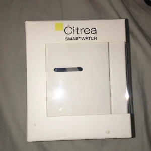 Citrea Smartwatch - Citrea Smartwatch med svart silikonarmband och magnetisk USB-laddkabel. Klockan har en modern, fyrkantig design och levereras i originalförpackning. Förpackningen har mindre slitage och en spricka, men klockan och tillbehör ser ut att vara i gott skick.