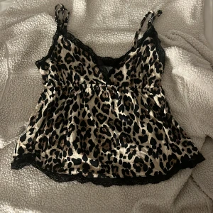 leopardlinne - Säljer en snygg linnetopp från Gina Tricot med leopardmönster i beige och svart. Toppen har tunna axelband, v-ringning och svarta spetsdetaljer längs kanterna. Materialet är glansigt och känns lyxigt mot huden. Perfekt för dig som vill sticka ut lite extra.