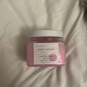 Sunday Rain Body Scrub Acai Berry - En rosa kroppsskrubb med acai berry-extrakt från Sunday Rain. Kommer i en fyrkantig plastburk med vitt lock och rymmer 265 g. Perfekt för att exfoliera huden och ge en fräsch känsla med bärdoft.