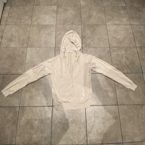 Ryvls Stockholm sip up tröja beige  - Snygg beige hoodie från Stajl med dragkedja framtill och huva med snörning. Tröjan har långa ärmar, ribbade muddar och två fickor på framsidan. Perfekt för chill dagar och enkel att matcha med jeans eller joggers.