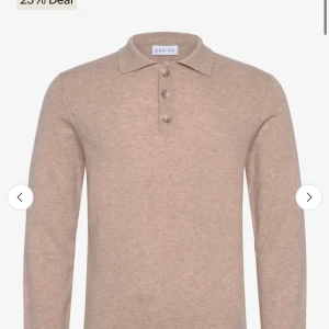 Beige pikétröja i kashmir från Davida - Säljer en stilren beige pikétröja från Davida i mjuk kashmir. Tröjan har klassisk krage, tre knappar framtill och lång ärm. Perfekt för dig som gillar en clean och lyxig look med extra komfort.