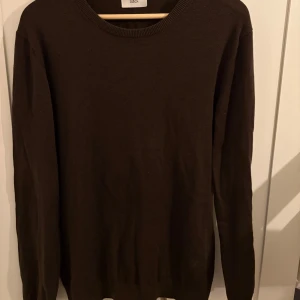 Mörkbrun stickad tröja från Bläck - En stilren mörkbrun stickad tröja från Bläck i storlek M. Tröjan har rund halsringning och långa ärmar, perfekt för lager-på-lager under kyliga dagar. Enkel och klassisk design som funkar till det mesta.