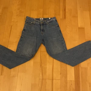 Blå jeans från Jack & Jones, stl 152 - Klassiska blå jeans från Jack & Jones i rak modell. Jeansen har fem fickor, gylf med dragkedja och knapp samt snygga kontrastsömmar. Tillverkade i slitstarkt bomullstyg, perfekta för en avslappnad och cool stil. 