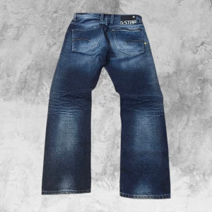 Rare G-Star RAW Vintage Grisch Bootcut Loose Distressed Y2K Blue Jeans Niche - De här jeansen från G-Star RAW har en fantastisk, autentisk tvätt och riktigt snygga slitningar från fabriken. Kolla bara in slitaget på knäna. De har den klassiska G-Star-kvaliteten och känslan, med en diskret bootcut som faller perfekt över skorna. Bakfickorna har den ikoniska G-Star-designen, komplett med den unika dragkedjedetaljen man inte ser varje dag.  Mått: Total längd – 105 cm Midja – 40 cm  Ett högkvalitativt fynd som absolut förtjänar en plats i din garderob :)