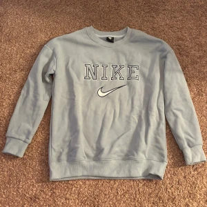 Ljusblå Nike sweatshirt i bomull - Säljer en ljusblå sweatshirt från Nike med klassisk logga och broderad text framtill. Tröjan har rund hals, långa ärmar och ribbade muddar. Perfekt för en chill och sportig look.