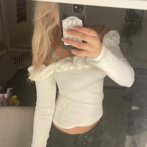 Vit offshoulder topp med volang - Säljer en superfin vit offshoulder topp med lång ärm och bred volang längs halsringningen. Toppen är tight och har en mjuk, stretchig känsla som sitter snyggt på kroppen. 