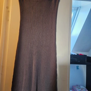 Brun ribbad långklänning Stories S - Säljer en brun långklänning från Stories i storlek S. Klänningen är ribbad och har en snygg, figurnära passform med bred linning upptill. Materialet är stickat och känns mjukt mot huden. Perfekt för dig som gillar stilrena och enkla plagg med lite edge. Oanvänd 