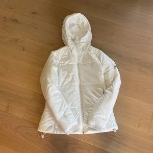 Vinterjacka - Säljer en  vit dunjacka från Adidas med huva och dragkedja framtill. Perfekt för kyliga dagar och enkel att matcha med olika outfits. Inga fläckar!