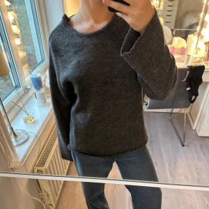 Mörkgrå stickad tröja med öppen rygg ifrån Ginatricot - Mysig mörkgrå stickad tröja med rund hals och långa ärmar. Tröjan har en snygg öppen rygg med knytband upptill, vilket ger en cool och unik look. Perfekt för lager-på-lager och chill dagar. Knappt använd