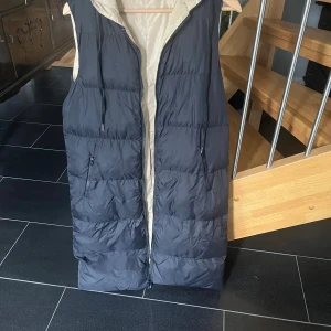 Lång pufferväst svart/beige - En svart/beige pufferväst i längre modell. Stl S