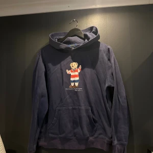 Mörkblå hoodie Polo Ralph Lauren S - Mörkblå hoodie från Polo Ralph Lauren i storlek XL barnstorlek. Passar som S.  ikonisk Polo Bear broderad på bröstet i röd, vit och blå tröja. Klassisk känguruficka och huva, perfekt för en chill och snygg look.