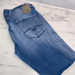 Replay Hyperflex ljusblå jeans - Säljer ett par Replay Hyperflex jeans i ljusblå tvätt med snygga slitningar och klassiska femficksdetaljer. Jeansen har raka ben och normal passform, med tydliga kontrastsömmar och logga på bakfickan. Perfekta för dig som gillar stilrena och bekväma jeans.
